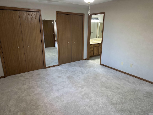 unfurnished bedroom featuring light carpet, two closets, ensuite bathroom, and sink