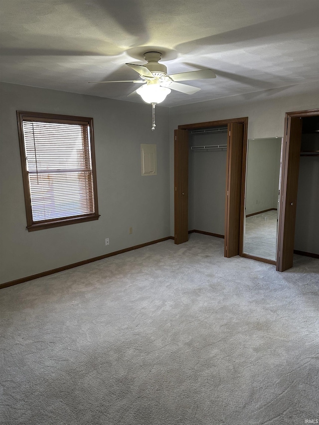 unfurnished bedroom featuring ceiling fan, light colored carpet, and multiple closets