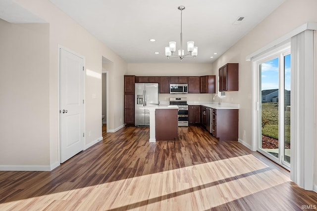 kitchen with appliances with stainless steel finishes, a center island, decorative light fixtures, and dark hardwood / wood-style flooring