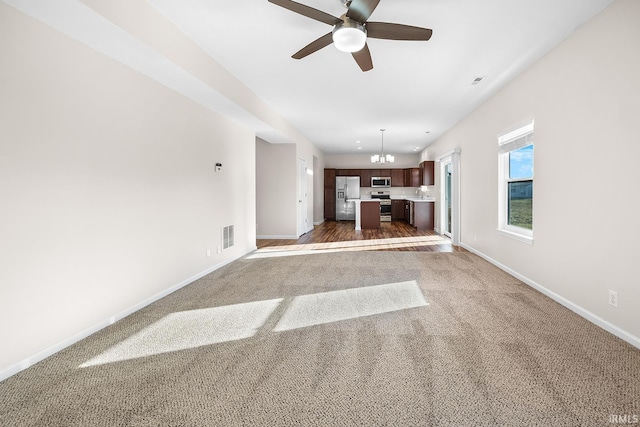 unfurnished living room with dark colored carpet and ceiling fan with notable chandelier