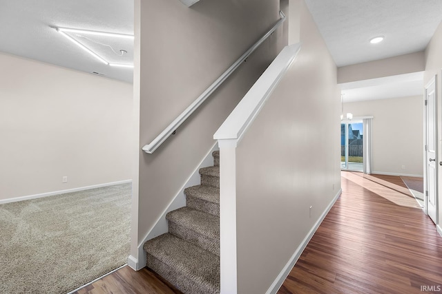 stairway featuring a chandelier, wood-type flooring, and a textured ceiling