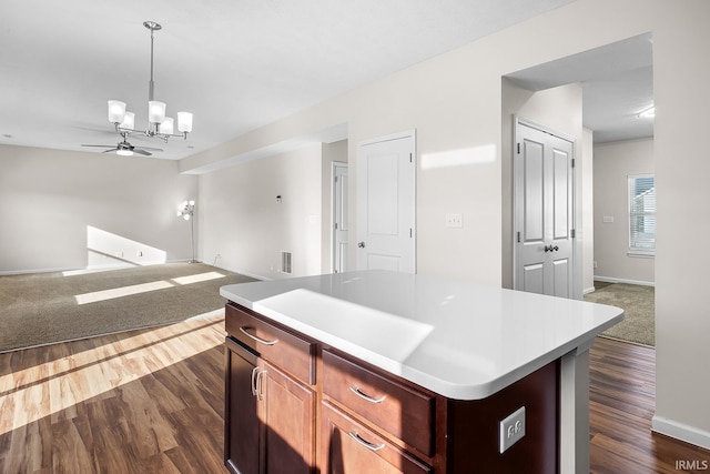 kitchen featuring ceiling fan with notable chandelier, a center island, dark hardwood / wood-style flooring, and hanging light fixtures