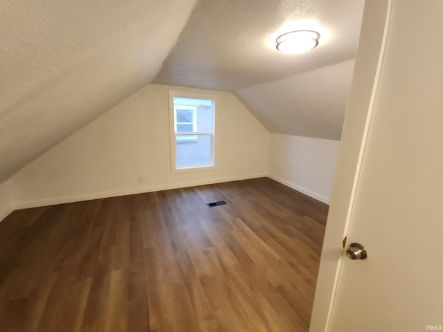 additional living space with hardwood / wood-style flooring, a textured ceiling, and vaulted ceiling