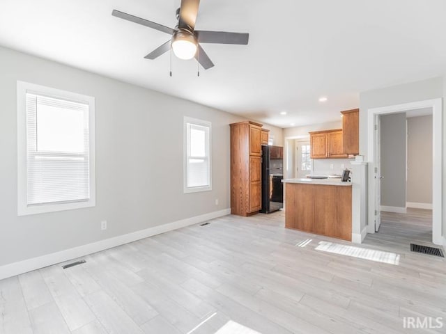 kitchen with kitchen peninsula, light hardwood / wood-style floors, black fridge, and plenty of natural light