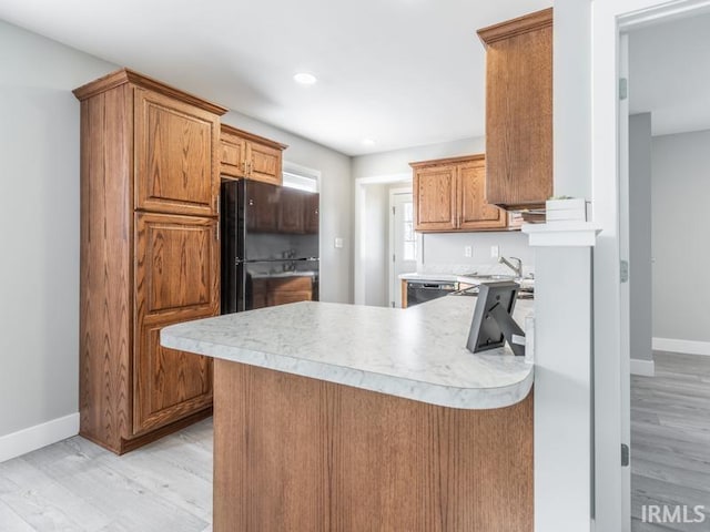 kitchen featuring black appliances, light hardwood / wood-style floors, kitchen peninsula, and sink