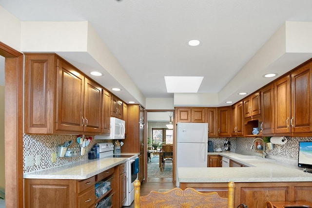 kitchen featuring white appliances, sink, a skylight, light wood-type flooring, and kitchen peninsula