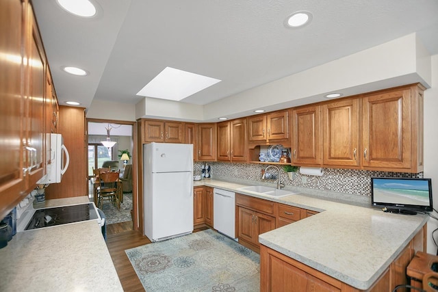 kitchen with a skylight, sink, light hardwood / wood-style flooring, kitchen peninsula, and white appliances