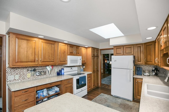 kitchen featuring a skylight, sink, dark wood-type flooring, backsplash, and white appliances