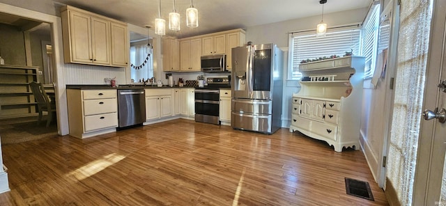 kitchen featuring pendant lighting, cream cabinetry, stainless steel appliances, and wood-type flooring