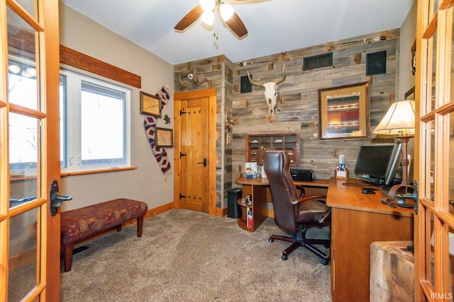 carpeted home office featuring ceiling fan, wood walls, and french doors