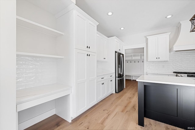 kitchen featuring appliances with stainless steel finishes, tasteful backsplash, premium range hood, white cabinets, and light hardwood / wood-style floors