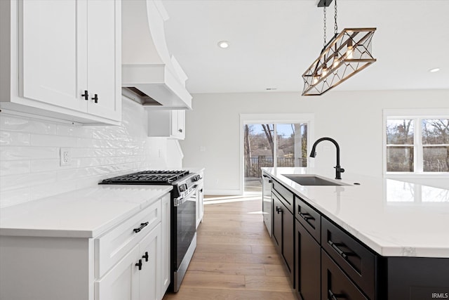 kitchen with appliances with stainless steel finishes, premium range hood, sink, light hardwood / wood-style flooring, and hanging light fixtures