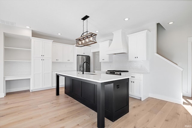 kitchen featuring a kitchen island with sink, light wood-type flooring, appliances with stainless steel finishes, tasteful backsplash, and custom range hood