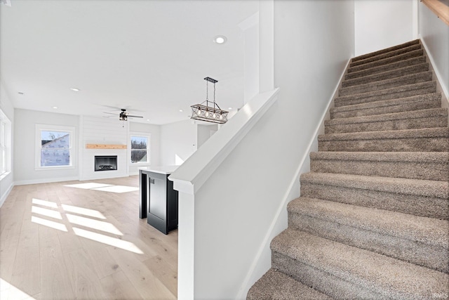 stairway featuring ceiling fan, a large fireplace, and wood-type flooring