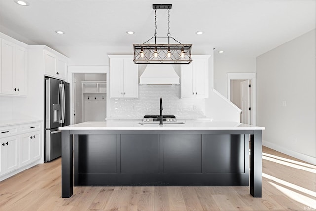 kitchen with hanging light fixtures, stainless steel appliances, a center island with sink, custom exhaust hood, and light wood-type flooring