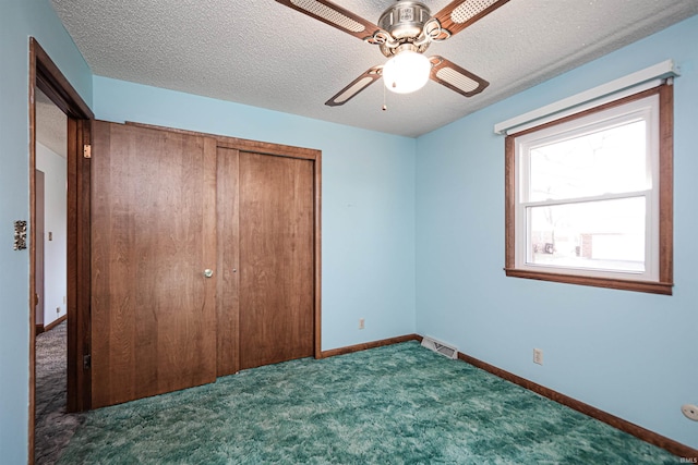 unfurnished bedroom with dark colored carpet, a textured ceiling, a closet, and ceiling fan