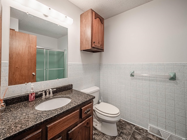 bathroom featuring tile patterned flooring, toilet, vanity, a shower with shower door, and tile walls