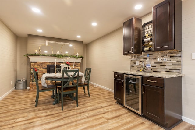 bar featuring light stone countertops, light wood-type flooring, tasteful backsplash, dark brown cabinetry, and beverage cooler