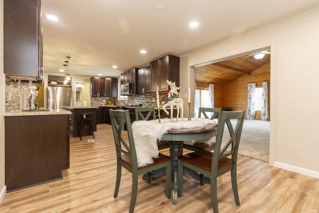 dining area with wood walls, light hardwood / wood-style floors, and lofted ceiling