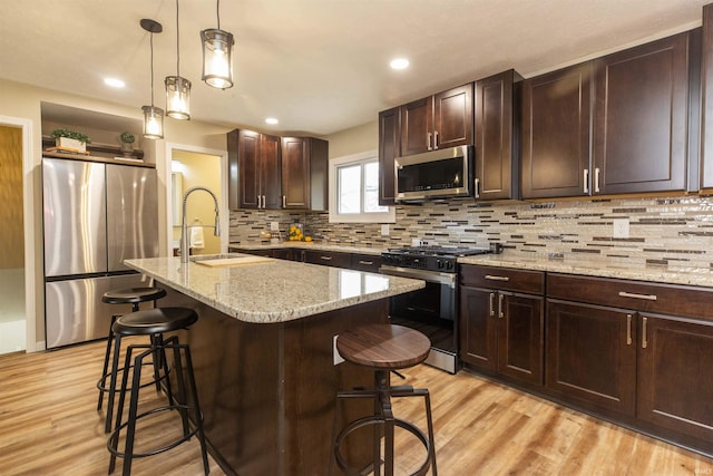 kitchen with a kitchen breakfast bar, a kitchen island with sink, light hardwood / wood-style floors, and appliances with stainless steel finishes