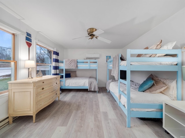 bedroom with ceiling fan, a wall mounted AC, and light hardwood / wood-style flooring