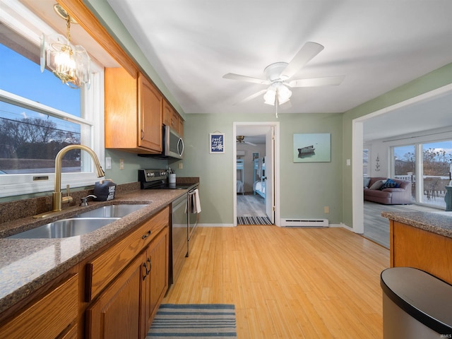 kitchen with appliances with stainless steel finishes, a baseboard heating unit, light hardwood / wood-style floors, sink, and hanging light fixtures