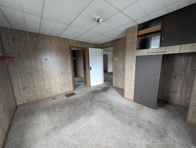 unfurnished room with a paneled ceiling, light colored carpet, and wood walls