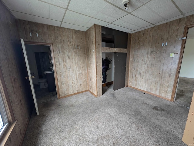 carpeted empty room with a paneled ceiling and wood walls