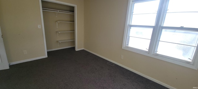 unfurnished bedroom with a closet, dark carpet, and multiple windows