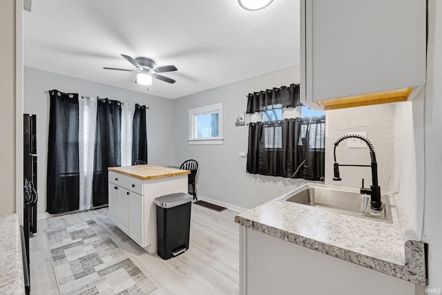 kitchen with wood counters, white cabinets, sink, light wood-type flooring, and a textured ceiling