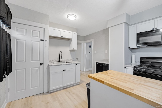 kitchen featuring butcher block counters, white cabinetry, sink, light hardwood / wood-style floors, and black appliances