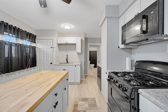 kitchen featuring light hardwood / wood-style flooring, white cabinetry, butcher block counters, and black appliances