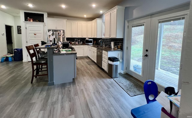 kitchen featuring decorative backsplash, light wood-type flooring, stainless steel appliances, a kitchen island, and white cabinetry