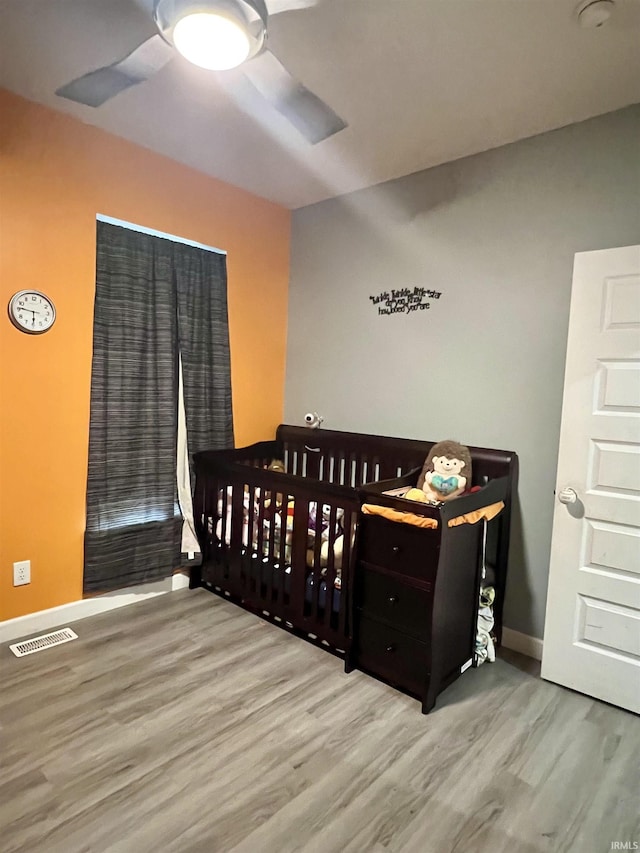 bedroom with a nursery area, light hardwood / wood-style floors, and ceiling fan