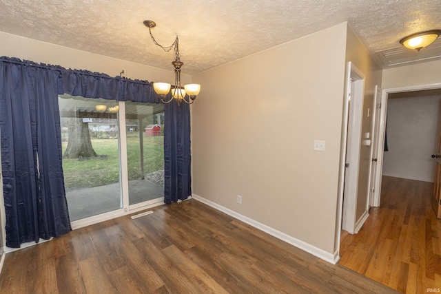 unfurnished dining area featuring a textured ceiling, a notable chandelier, and dark wood-type flooring