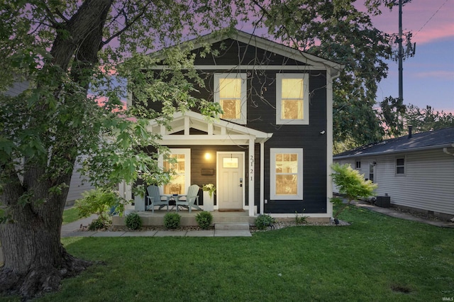 back house at dusk featuring a lawn and covered porch