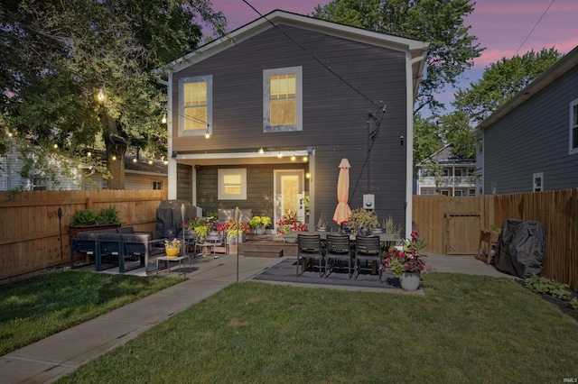 back house at dusk featuring a yard and a patio area