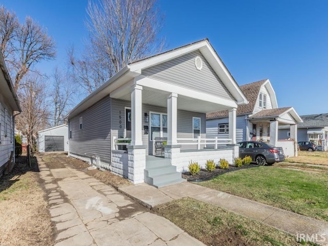 bungalow-style home featuring a garage, covered porch, an outbuilding, and a front yard