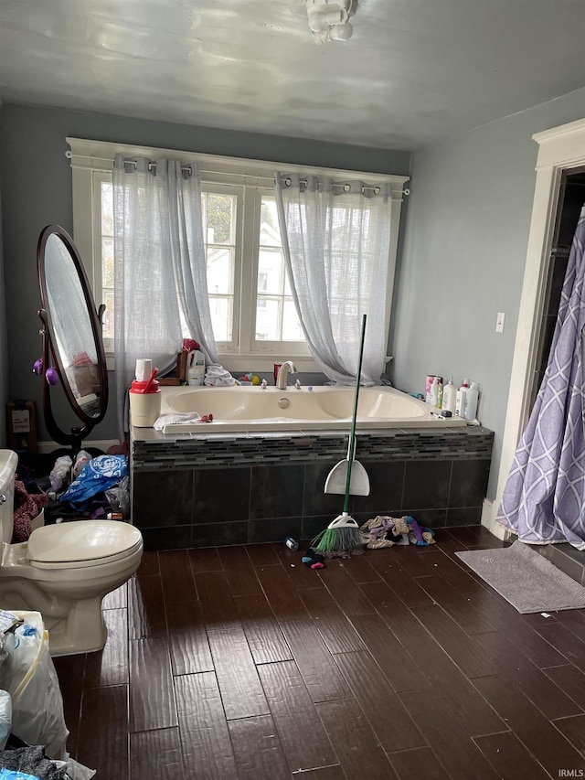 bathroom with wood-type flooring, a relaxing tiled tub, and toilet