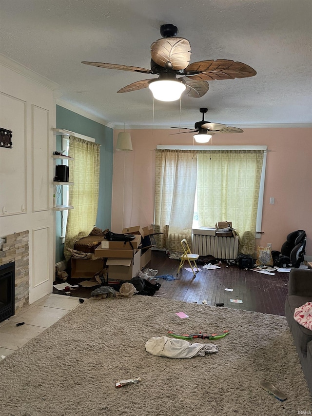 interior space featuring a stone fireplace, ceiling fan, light wood-type flooring, a textured ceiling, and ornamental molding