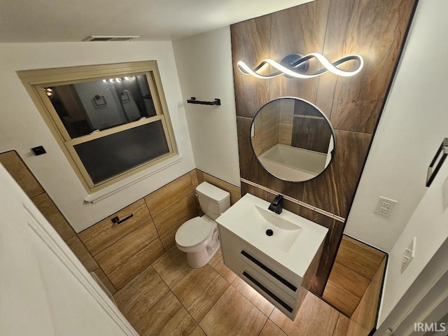 bathroom with tile patterned floors, vanity, vaulted ceiling, tile walls, and toilet