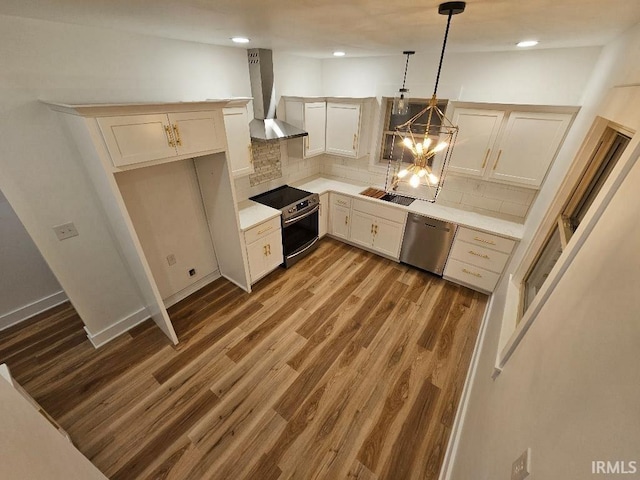 kitchen with dark wood-type flooring, wall chimney exhaust hood, decorative backsplash, decorative light fixtures, and stainless steel appliances