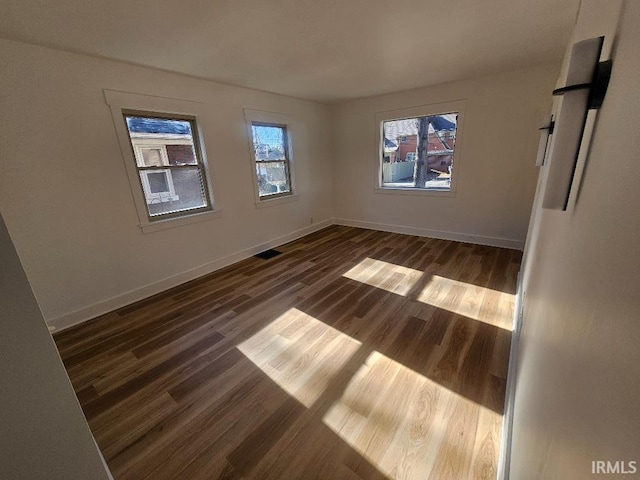 spare room with dark hardwood / wood-style flooring and a healthy amount of sunlight