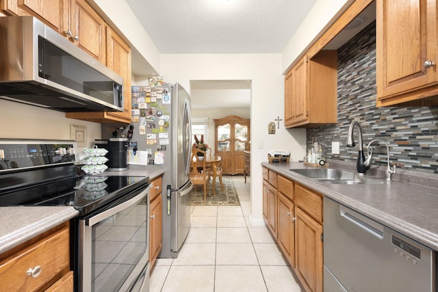 kitchen featuring sink, backsplash, a textured ceiling, light tile patterned flooring, and appliances with stainless steel finishes