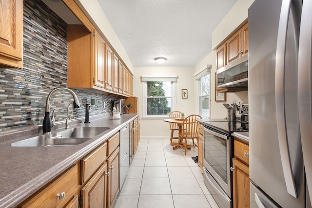 kitchen featuring sink, light tile patterned floors, a textured ceiling, appliances with stainless steel finishes, and tasteful backsplash