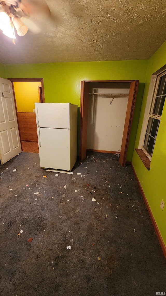 unfurnished bedroom featuring dark colored carpet, ceiling fan, white refrigerator, and a textured ceiling