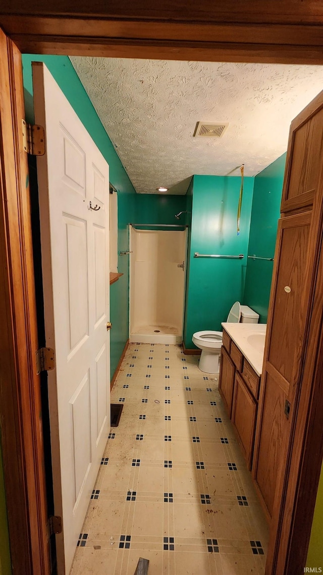 bathroom featuring toilet, vanity, a textured ceiling, and walk in shower