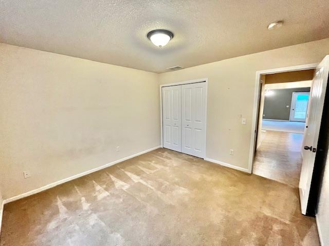 unfurnished bedroom with light colored carpet, a textured ceiling, and a closet