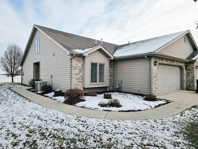 snow covered property featuring a garage and central air condition unit