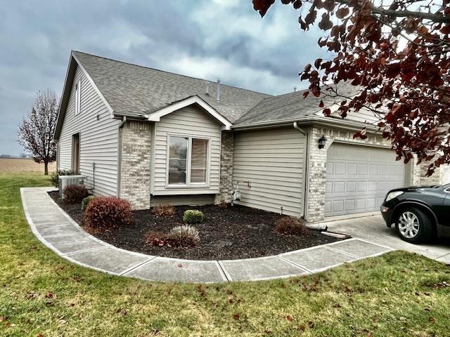 view of front of home featuring a front lawn, central AC unit, and a garage